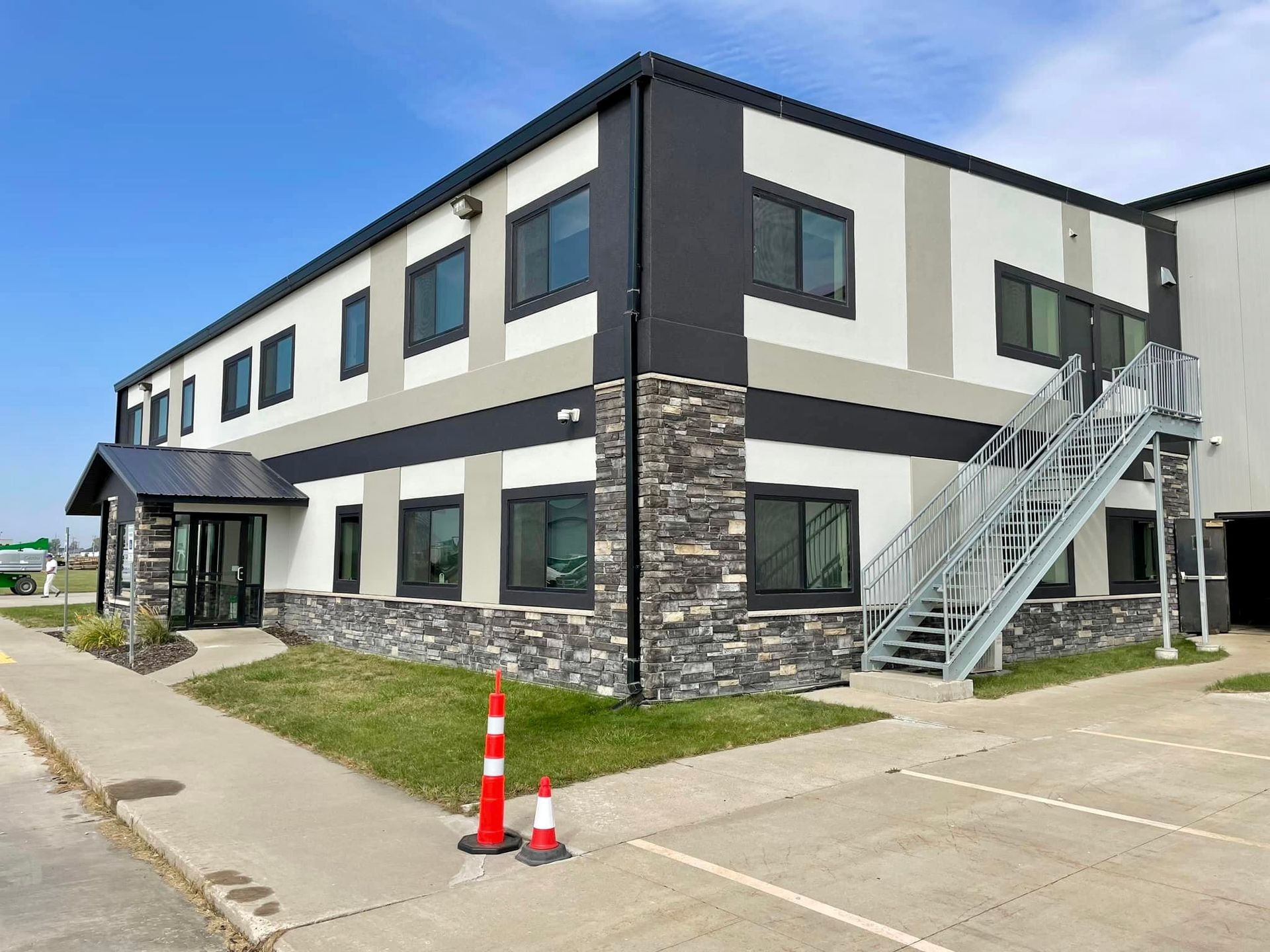 Two-story building with stone facade, metal stairs, and a black roof under a blue sky.